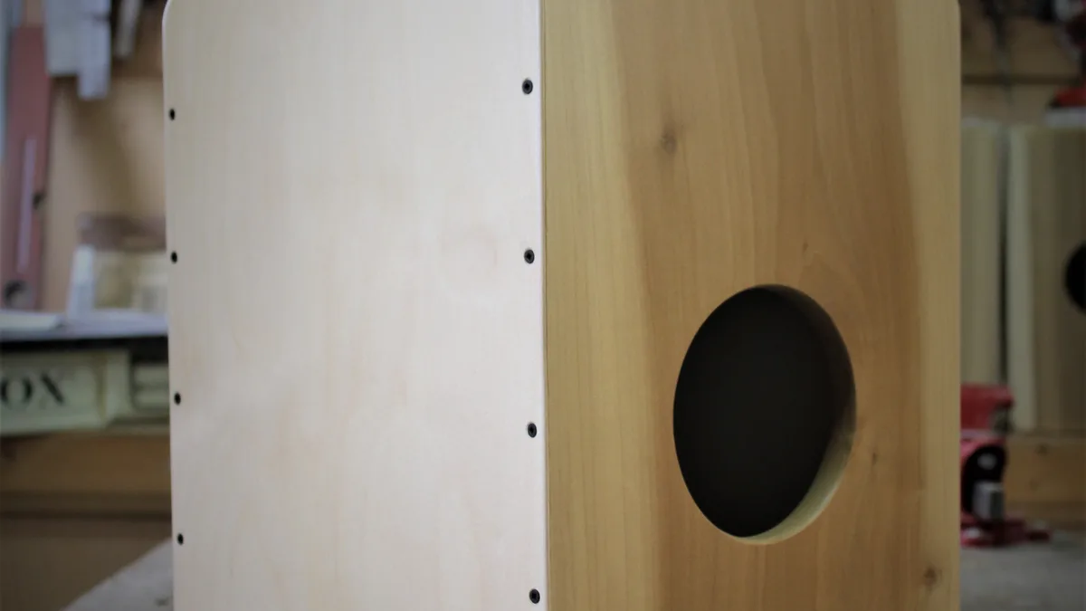 Primer plano de un cajón de madera clara en un taller, con la tapa lisa a un lado y la boca redonda de la cara trasera
