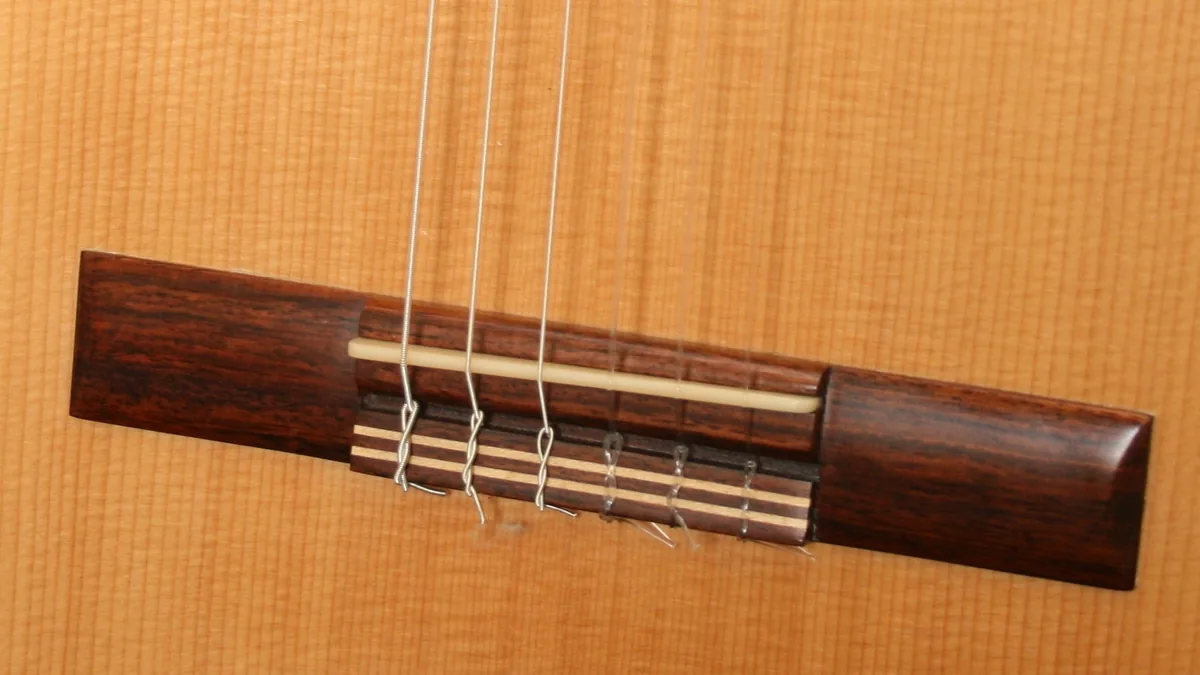 Puente de una guitarra clásica con la selleta de hueso sobre la que apoyan las cuerdas de nailon